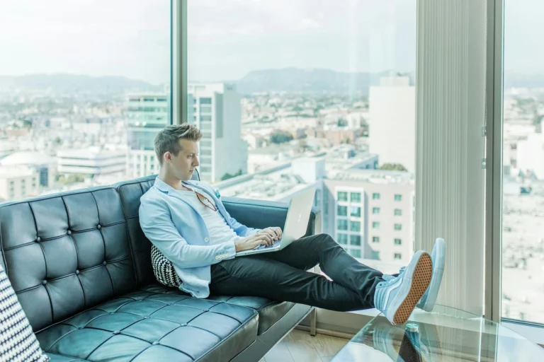 Junger Berufstätiger, der sich über finanzielle Absicherung und Dienstunfähigkeit informiert, während er auf einem Laptop in einem modernen Büro mit Stadtblick arbeitet.