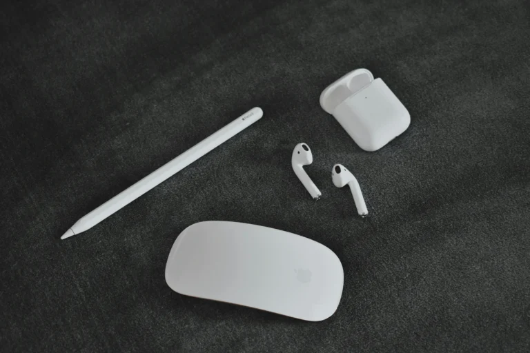 Verschiedene Apple-Zubehörteile für Studierende auf einem dunklen Untergrund, darunter ein Apple Pencil, AirPods in ihrem Ladeetui und eine Magic Mouse.