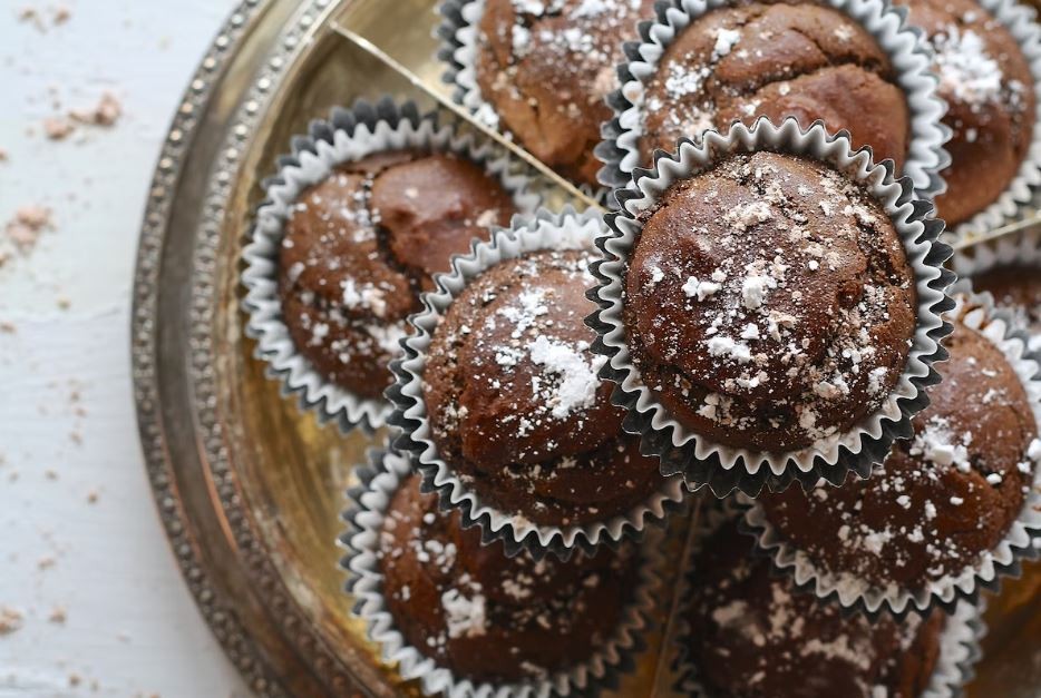 A plate of chocolate muffins stacked high and covered in icing sugar as another example of summer finger foods. Vaia Magazine